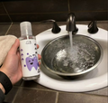 Person holding a bottle labeled 'PawRight' over a sink with water flowing.