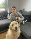 Woman holding PawBright Dental Plus and a dog on a couch with another dog sitting nearby.
